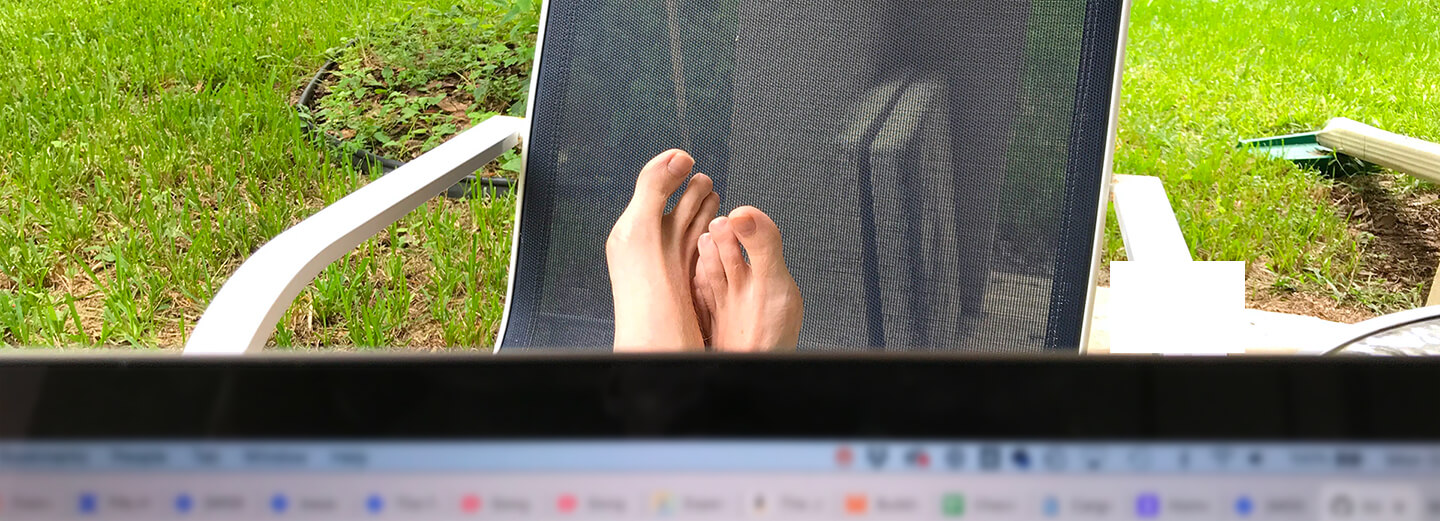 The blurry edge of a laptop in the foreground obscuring bare feet on a lawn chair